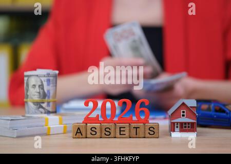 Conte degli asset e pianificazione finanziaria per il 2026 con contanti, una casa modello e una macchinina giocattolo Foto Stock