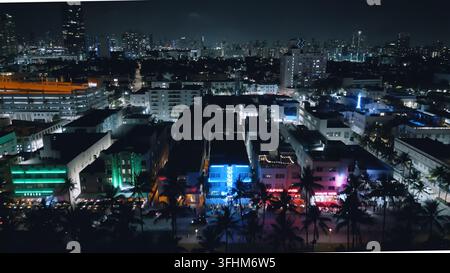 Vista aerea degli hotel Art Deco illuminati al neon lungo Collins Avenue con palme e lo skyline della città di notte a Miami Beach, Florida, Stati Uniti. Foto Stock