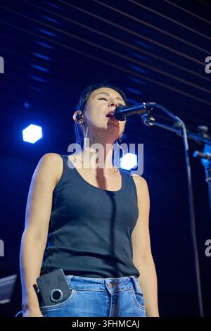 Giovane cantante con capelli scuri canta in un microfono durante il sound check della band sul palco del concerto, sotto i fari blu e accanto all'attrezzatura audio Foto Stock