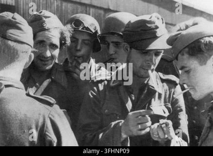 Soldati tedeschi che si riposano e fumano sigarette, uno tiene un piccolo oggetto, forse un accendino o una scatola di fiammiferi, settembre 1944. Foto Stock