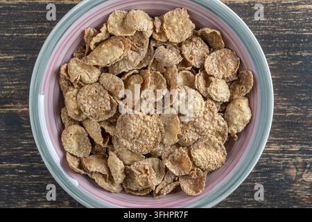 Fiocchi smaltati a grana intera in piastra, primo piano, vista dall'alto. Colazione sana, muesli a grani interi in una ciotola Foto Stock