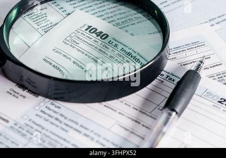 Vista ravvicinata del modulo fiscale statunitense 1040 con una lente d'ingrandimento e una penna sopra, che suggerisce la preparazione e la dichiarazione dei redditi per la stagione fiscale. Foto Stock