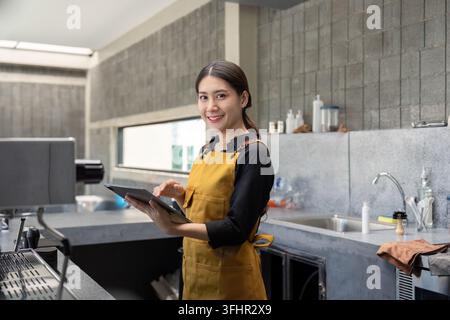 Giovane barista in un moderno Coffee Shop che tiene un tablet e sorride alla fotocamera Foto Stock