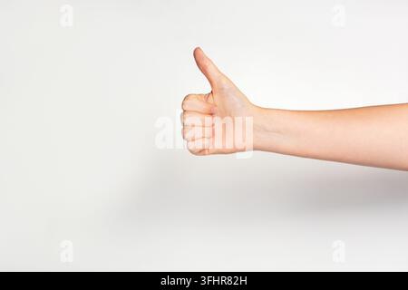 La mano di una donna che gestiva i pollici mostrando buona o ok su sfondo grigio chiaro. Foto Stock