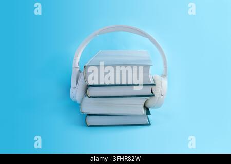 Cuffie wireless bianche su una pila di libri su sfondo azzurro. Concetto per audiolibri in stile minimalista Foto Stock