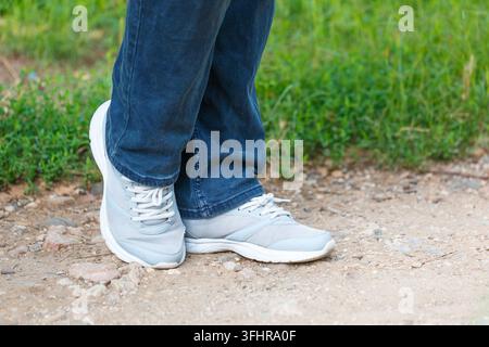 Gambe di uomo in scarpe da ginnastica luminose si ergono sulla strada nel parco sullo sfondo Foto Stock