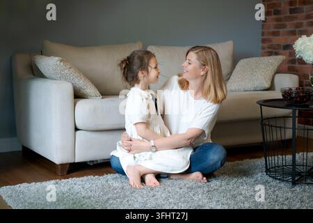 Nonna e nipote felici sono sedute insieme sul pavimento accogliente vicino al divano Foto Stock