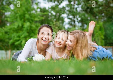Famiglia allegra nel parco, mamma e figlia e nonna sdraiate sull'erba verde Foto Stock