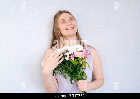 Una donna tiene un mazzo di fiori e sorride Foto Stock