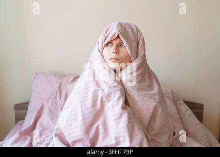 Una donna è avvolta in una coperta rosa e guarda verso la fotocamera Foto Stock