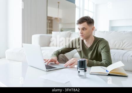 Un uomo è seduto su un divano e lavora su un laptop Foto Stock