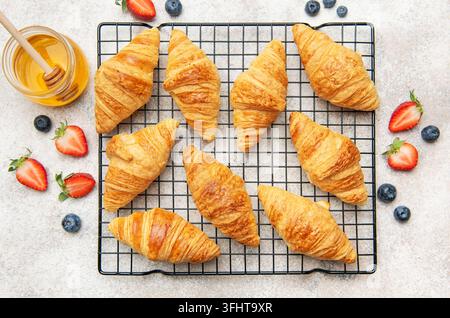 Croissant appena sfornati che si raffreddano su una griglia con miele e bacche Foto Stock