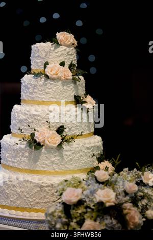 Elegante torta nuziale bianca a più piani decorata con rose pesche e nastro dorato Foto Stock