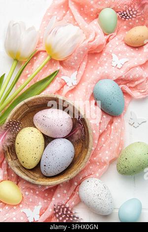 Sfondo pasquale con uova colorate in una ciotola e tulipani rosa Foto Stock