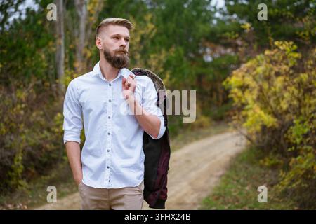 Ritratto di un giovane uomo barbuto che cammina sulla strada nel parco in autunno. Foto Stock