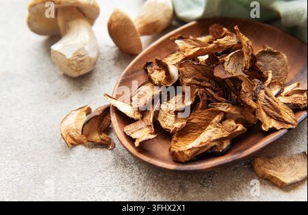 Funghi porcini essiccati riposti in una ciotola di legno su uno sfondo grigio ruvido Foto Stock
