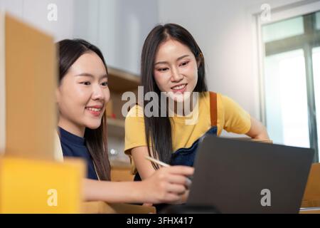 Due donne si impegnano in attività di e-commerce, dimostrando lavoro di squadra e competenze digitali in un ambiente d'ufficio vivace. Foto Stock