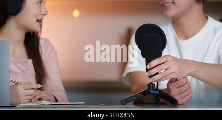 Due giovani adulti si impegnano in una vivace interazione podcast, mostrando lavoro di squadra e creatività in un ambiente informale. Foto Stock