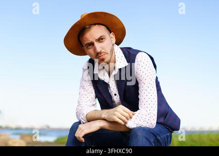 Ritratto di un giovane uomo adulto con cappello, camicia bianca e gilet sullo sfondo della natura Foto Stock