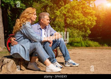 Coppia matura al lago con una bicicletta seduta al sole Foto Stock