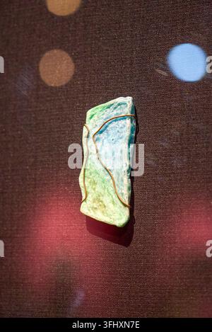 Il ciondolo in pezzo di minerale verde e bianco è avvolto e fissato con filo di rame, e la trama artigianale è evidenziata sullo sfondo di tessuto scuro Foto Stock