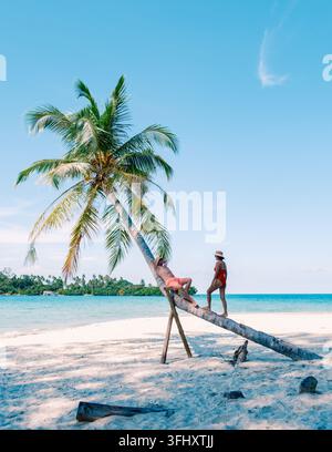 Due amici si godranno una giornata di divertimento all'isola di Koh Kood, rilassandosi su una palma vicino al vibrante mare blu. Il caldo sole splende sull'idilliaco para tropicale Foto Stock