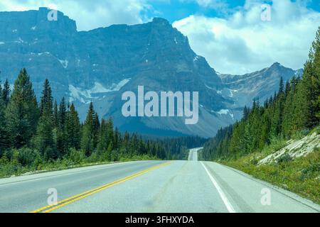 Un'autostrada asfaltata si snoda attraverso una fitta foresta sempreverde con maestose montagne rocciose, distretto di miglioramento n. 9 Banff, Alberta, Canada Foto Stock