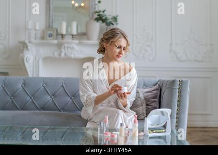 Giovane donna felice che tiene una crema idratante per il viso e sorride mentre applica la crema Foto Stock