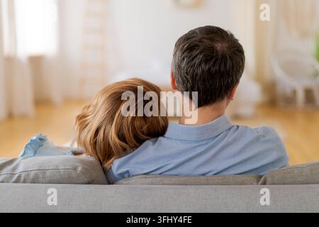 Una coppia che si abbraccia e si siede su un divano, vista da dietro Foto Stock
