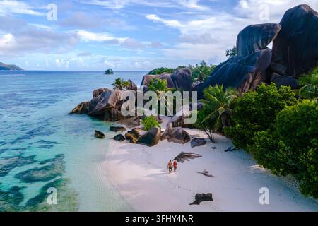 Coppia che si gode una romantica passeggiata lungo la splendida spiaggia Anse Source d'Argent a la Digue, Seychelles. Palme lussureggianti e rocce di granito creano una tropica Foto Stock