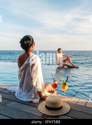 Un momento sereno presso la piscina a sfioro di Willemstad, Curacao. Due viaggiatori si godono cocktail rinfrescanti mentre il sole tramonta sul Mar dei Caraibi, creando Foto Stock