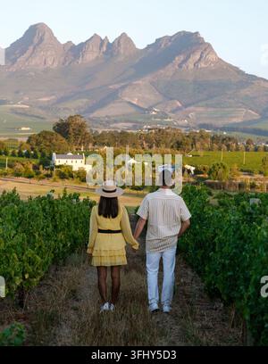 La coppia gode di un momento sereno camminando mano nella mano attraverso lussureggianti vigneti circondati da splendide montagne a Stellenbosch. Ambiente ideale per un romantico Foto Stock