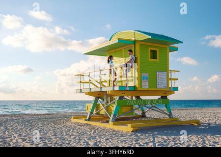 La torre gialla del bagnino si erge a guardare Miami Beach mentre le persone si rilassano sulla sabbia calda, godendo della splendida vista costiera e dell'atmosfera vibrante Foto Stock