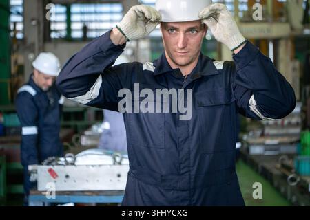 Capo squadra industriale in piedi in una fabbrica di produzione con operai che azionano macchinari sullo sfondo, rappresentando il lavoro di squadra e le pubbliche relazioni industriali Foto Stock