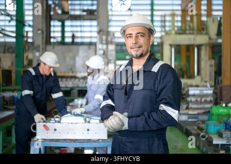 Capo squadra industriale in piedi in una fabbrica di produzione con operai che azionano macchinari sullo sfondo, rappresentando il lavoro di squadra e le pubbliche relazioni industriali Foto Stock