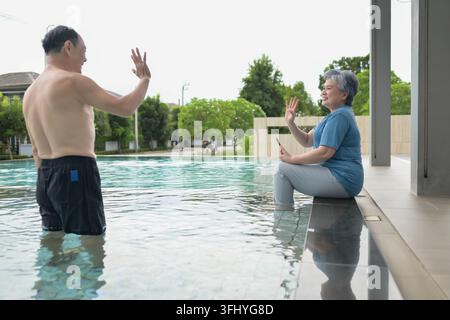 Coppia di anziani che gioca con l'acqua in una piscina, creando un'atmosfera gioiosa e rilassata Foto Stock