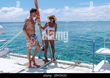 Una coppia elegante si rilassa su un catamarano a Mauritius, circondato da splendide acque turchesi. Il sole luminoso illumina le loro espressioni gioiose come Foto Stock