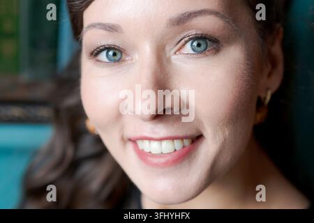 Primo piano estremo di una giovane donna felice con un sorriso radioso e occhi blu. Luce naturale soffusa, sfondo sfocato. Concetto di felicità, dentale lui Foto Stock