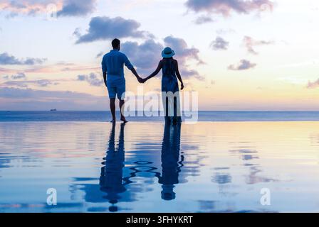 Una coppia amorevole cammina mano nella mano attraverso le calme acque di Santa Lucia durante un tramonto mozzafiato. Il cielo è dipinto in tonalità vibranti, creando un Foto Stock