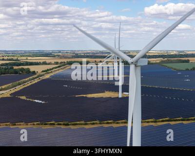 Turbinie eoliche bianche si ergono in un grande parco solare mentre l'elettricità pulita viene generata sotto un cielo diurno luminoso con soffici nuvole sparse Foto Stock