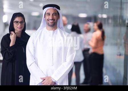 Professionisti aziendali mediorientali e arabi in un moderno ufficio open-plan, uomo emiratino sorridente in tradizionale kandura e collega donna in abaya Foto Stock