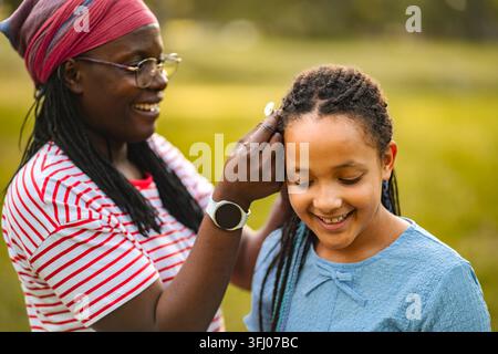 Madre afroamericana che acconcia i capelli della figlia all'aperto creando un legame Foto Stock
