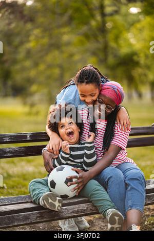 Felice famiglia afroamericana che ride seduto sulla panchina del parco Foto Stock