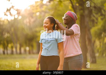 Madre che intreccia i capelli della figlia nel parco al tramonto Foto Stock