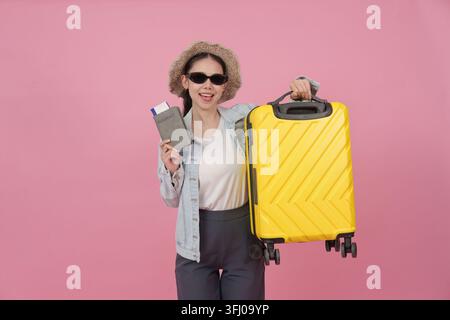 Felice viaggiatrice asiatica con passaporto, biglietti e bagagli gialli Foto Stock