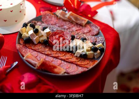 Piatto di salumi con formaggio, olive e carni stagionate. Piatto di salumi con varie carni stagionate, formaggi e olive nere su un rosso romantico Foto Stock