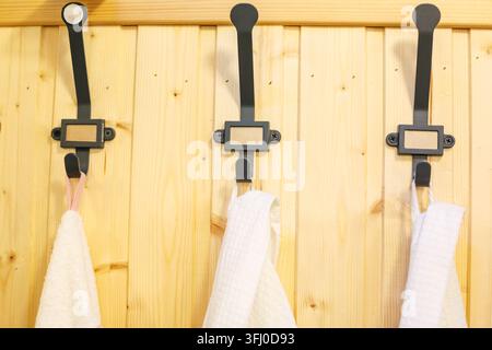 Tre ganci in metallo nero con asciugamani di cotone bianco appesi a una parete in legno di pino nel bagno Foto Stock
