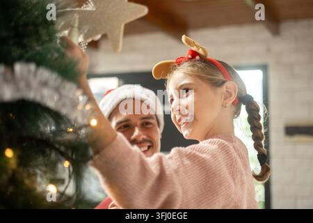 Padre e figlia decorano insieme l'albero di Natale a casa Foto Stock