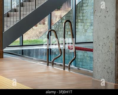 Il design minimalista definisce una piscina coperta moderna con ringhiere in acciaio inossidabile, pavimentazione in legno ed elementi in cemento per trasmettere una sofisticazione Foto Stock