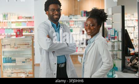 Due farmacisti medici afroamericani, uomo e donna, che lavorano con diagnosi sanitarie, sorridendo, guardando la telecamera, lavorano in una farmacia Foto Stock